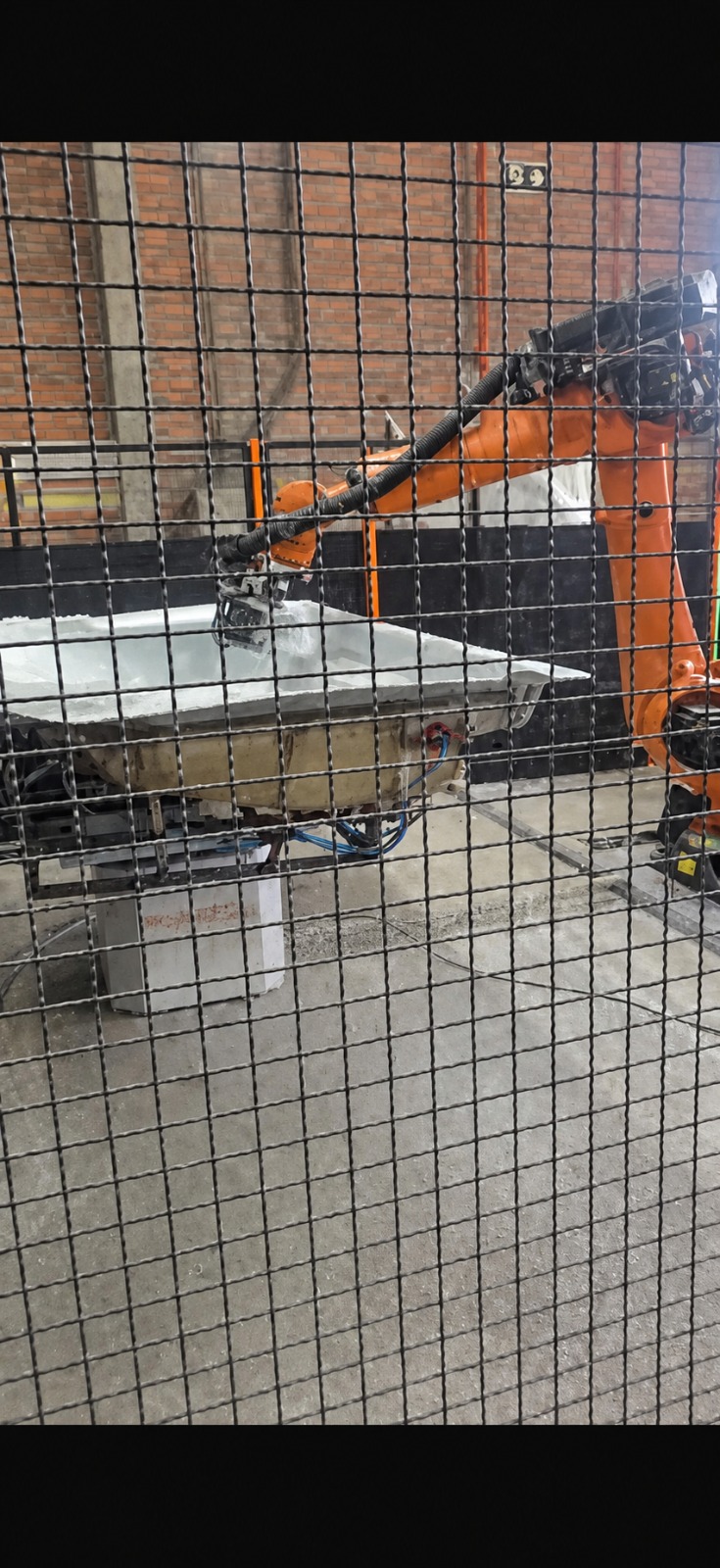 Robô industrial trabalhando em peça dentro da célula da Elobras